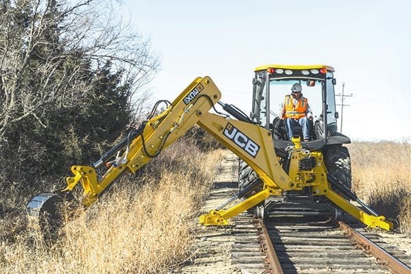 JCB backhoe loader equipped with Dymax Rail Rider BL hi-rail system on railroad track