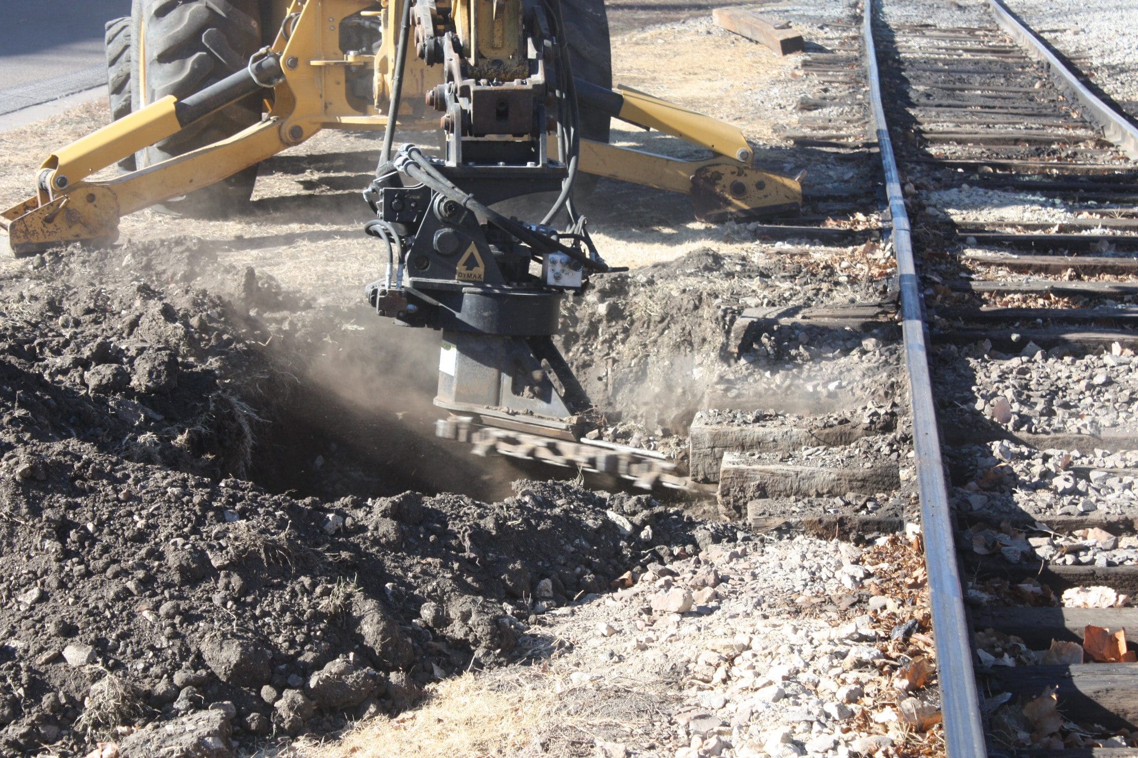 Ballast Blaster Cutter Bar – Active Undercutting in Heavily Fouled Ballast DymaxRail Ballast Blaster cutter bar cutting horizontally through heavily fouled ballast and mud beneath railway ties, showing active material removal with rotation housing and carbide chain