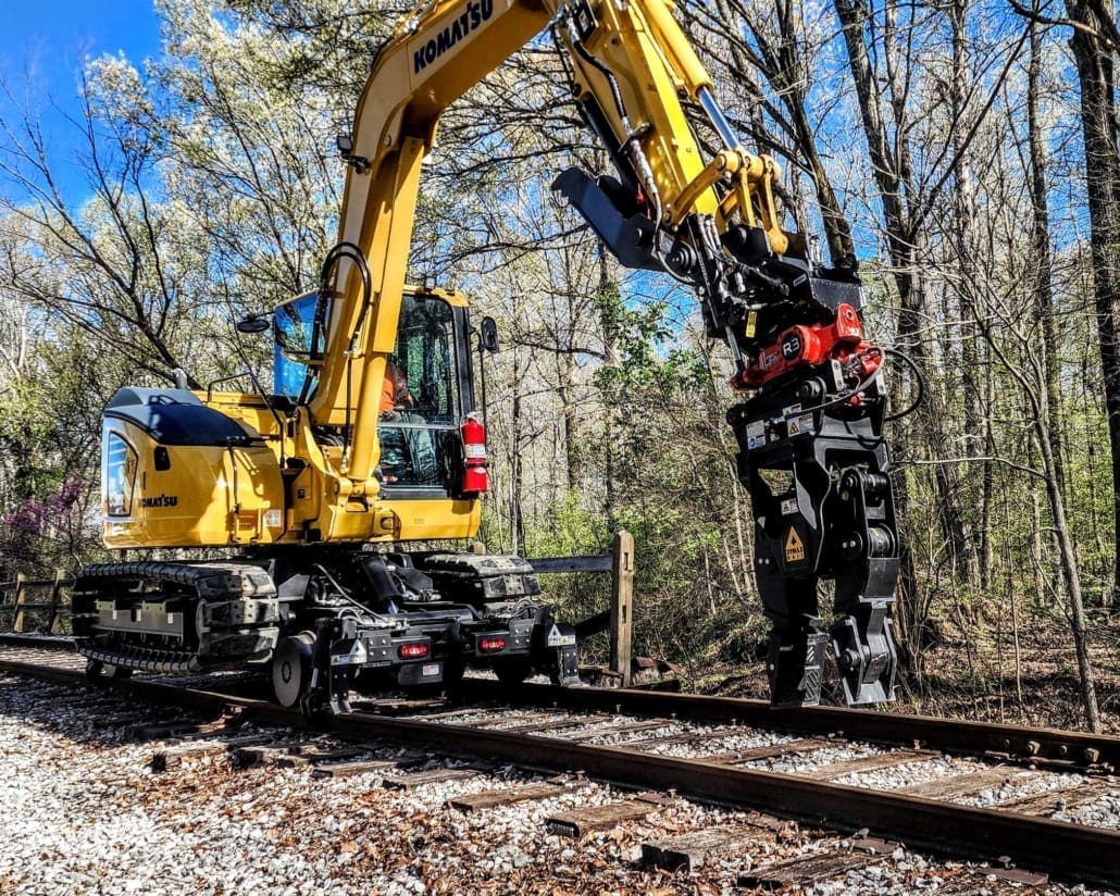 Komatsu 8-ton excavator with Dymax Rail Rider 8T hi-rail system and tiltrotator Komatsu 8-ton track excavator on the Dymax Rail Rider 8T hi-rail system fitted with a Rototilt R3 tiltrotator and grapple working a wooded rail right-of-way