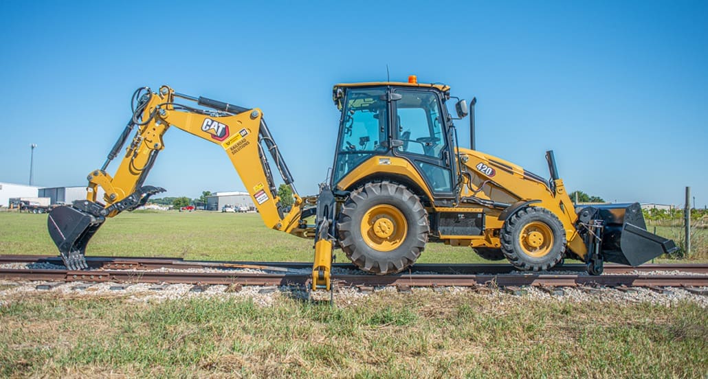 Caterpillar 420 backhoe loader with DymaxRail Rail Rider S-BL stabilizer-mounted hi-rail system on railroad track