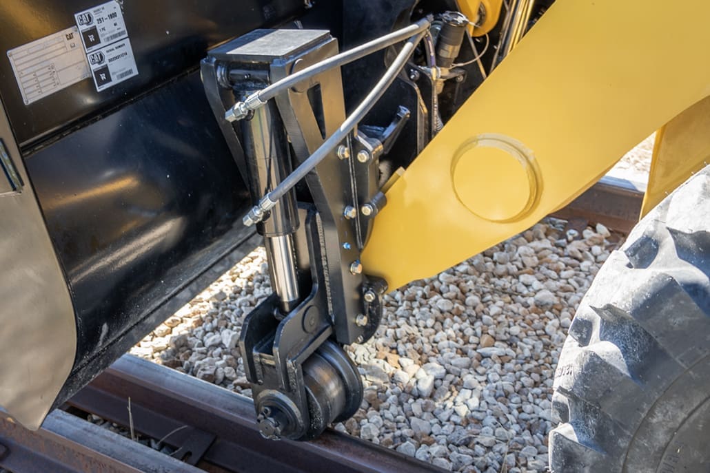 DymaxRail Rail Rider S-BL front coupler-mounted hydraulic-lift rail guide kit on Caterpillar 420 backhoe, showing 7-inch rail wheels deployed for on-track guidance