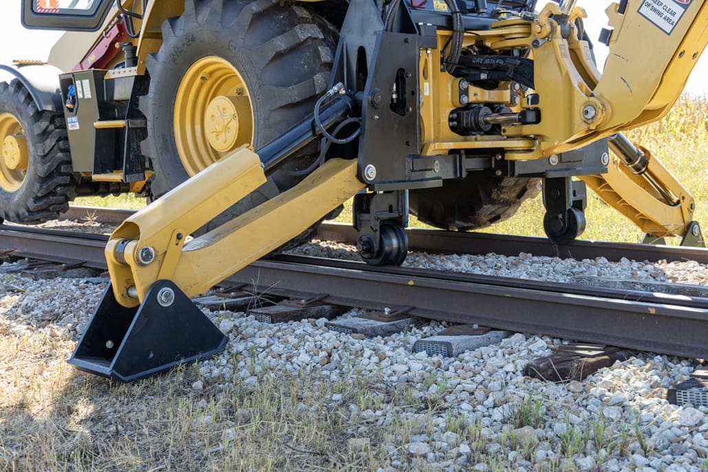 Caterpillar 420 backhoe loader with DymaxRail Rail Rider S-BL stabilizer-mounted hi-rail system, side view showing stabilizer railgear deployed on track