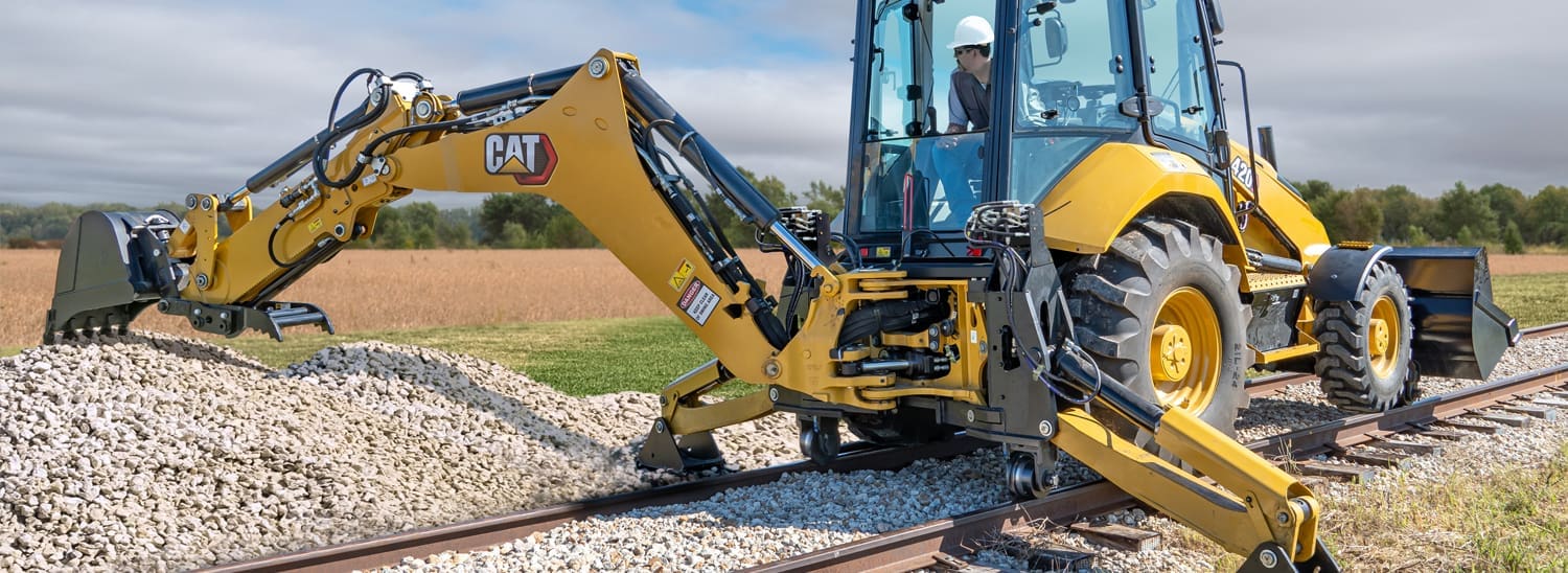 Dymax Rail Rider S-BL stabilizer-mounted hi-rail system installed on Caterpillar backhoe loader on railroad track