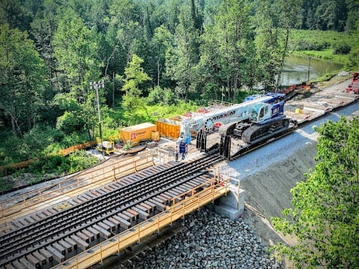 Click to show details - DymaxRail 100T Machinery Rail Cart – Kiewit Bridge Replacement DymaxRail 100-ton machinery rail cart transporting heavy equipment for Kiewit bridge replacement project