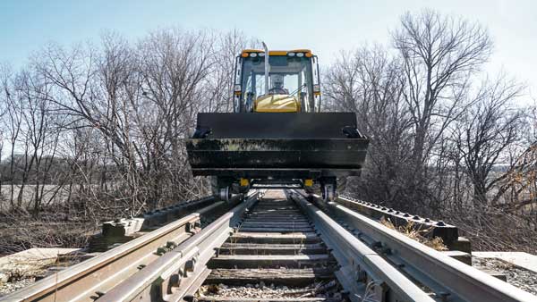 Backhoe loader with the Dymax Rail Rider hi-rail guide system crossing a bridge on railroad track