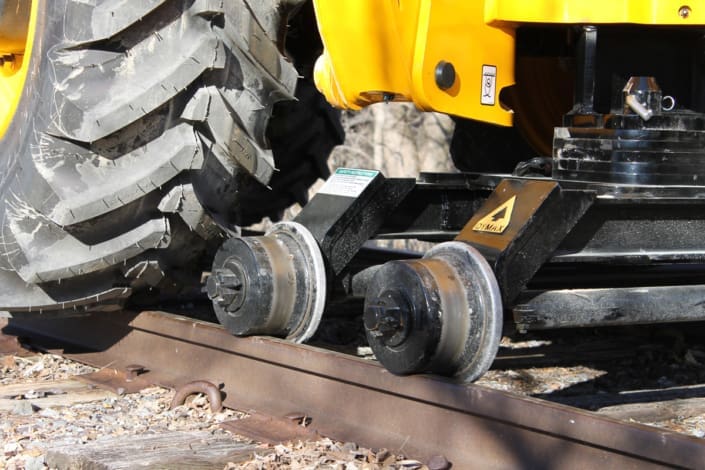 Close-up of the Dymax Rail Rider rear dolly supporting a backhoe loader on rail