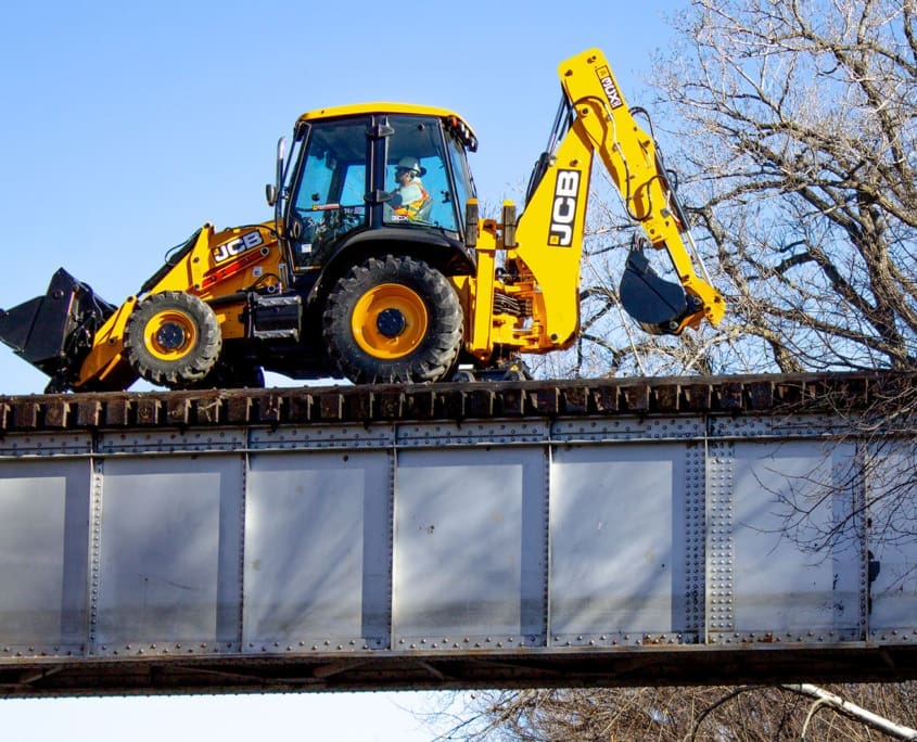 DymaxRail Rail Rider BL Hi-Rail System – JCB Backhoe Loader DymaxRail Rail Rider BL hi-rail system on JCB backhoe loader crossing railroad bridge