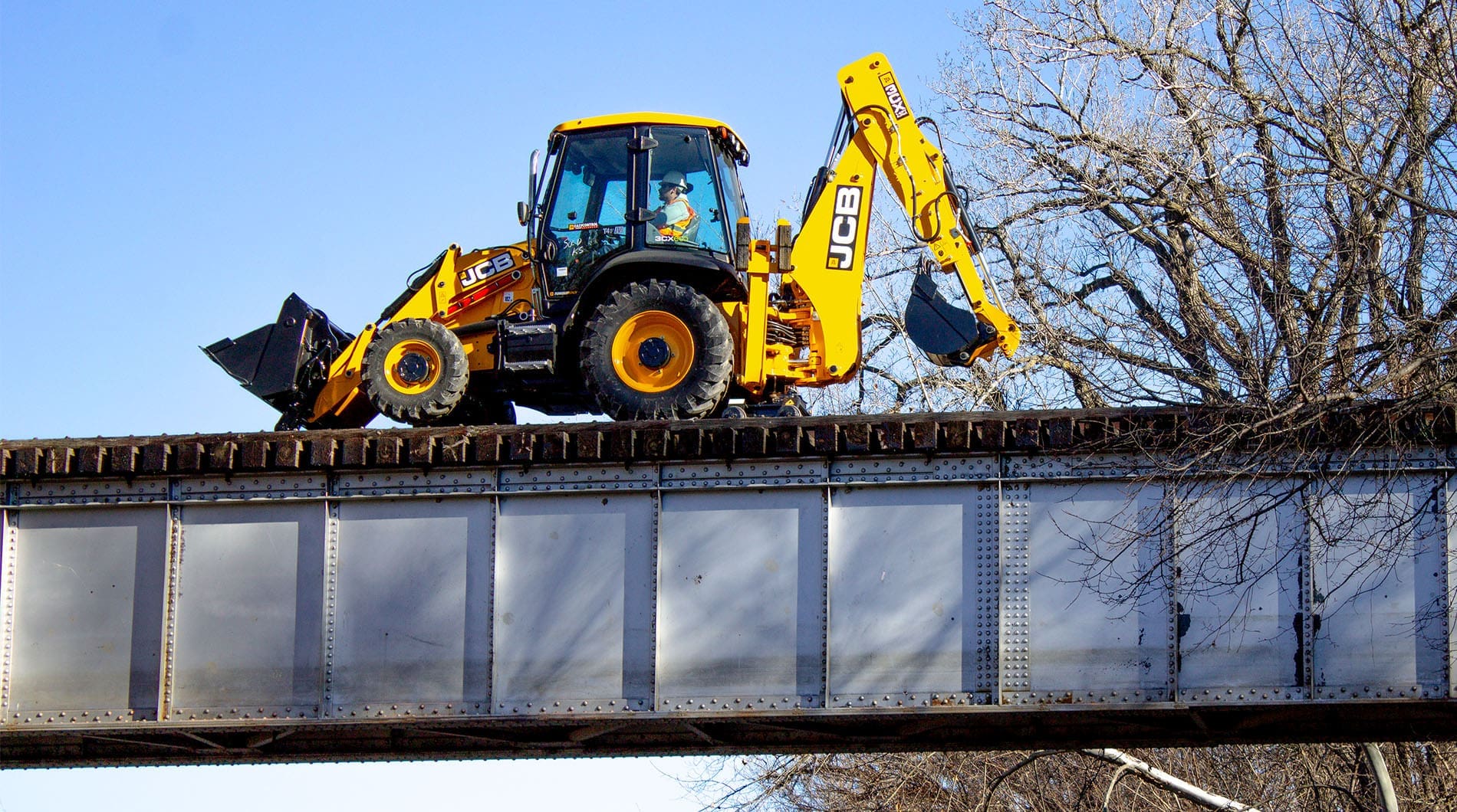 Backhoe loader equipped with the Dymax Rail Rider hi-rail guide system traveling on railroad track