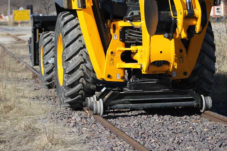 Standard backhoe loader fitted with the Dymax Rail Rider hi-rail guide system in rail application