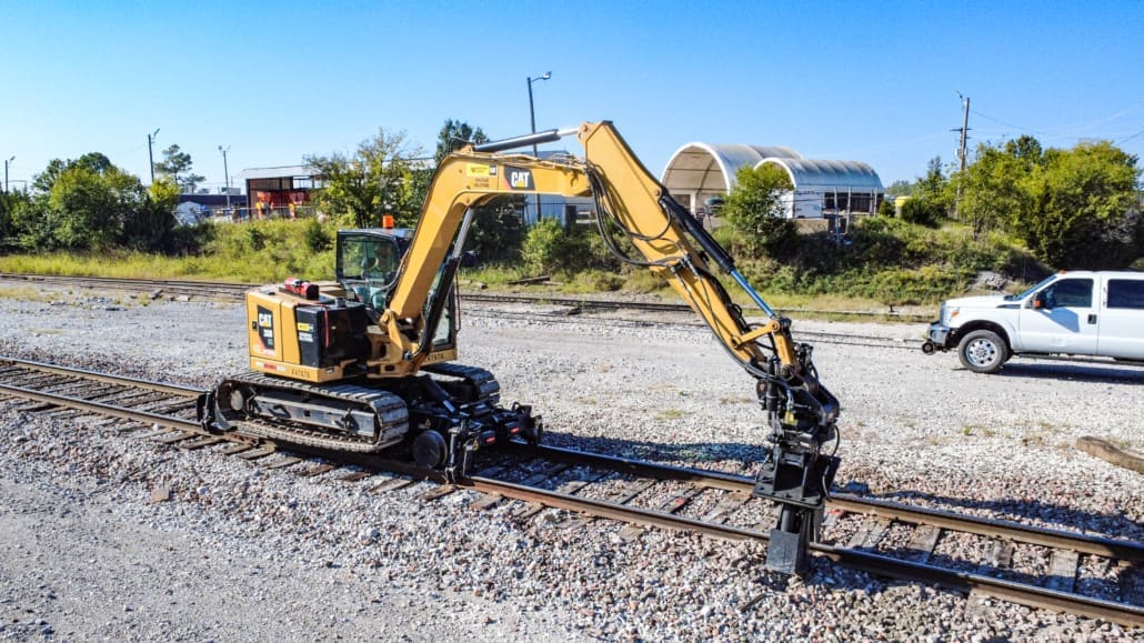 Cat 8-ton track excavator with Dymax Rail Rider X2-8T hi-rail system Cat 8-ton track excavator equipped with the Dymax Rail Rider X2-8T hi-rail system working in a railroad maintenance yard