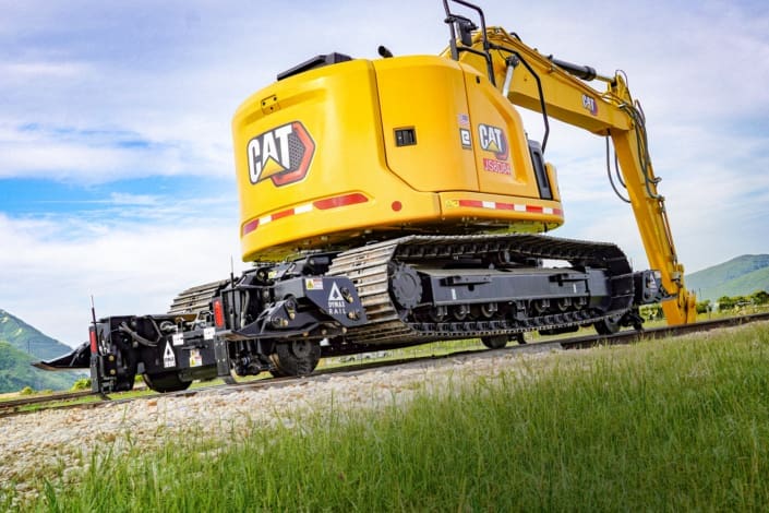 Cat 315 track excavator with Dymax Rail Rider X2-15T hi-rail attachment on rail Cat 315 track excavator equipped with the Dymax Rail Rider X2-15T detachable hi-rail attachment on rail, shown from the rear with the modular hi-rail assemblies fully supporting the machine