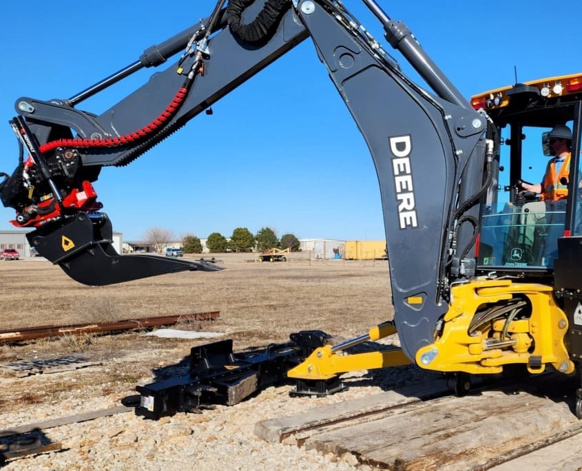 DymaxRail 8-inch cribbing bucket mounted on John Deere 710P backhoe loader with Rail Rider hi-rail attachment, railway track maintenance operation
