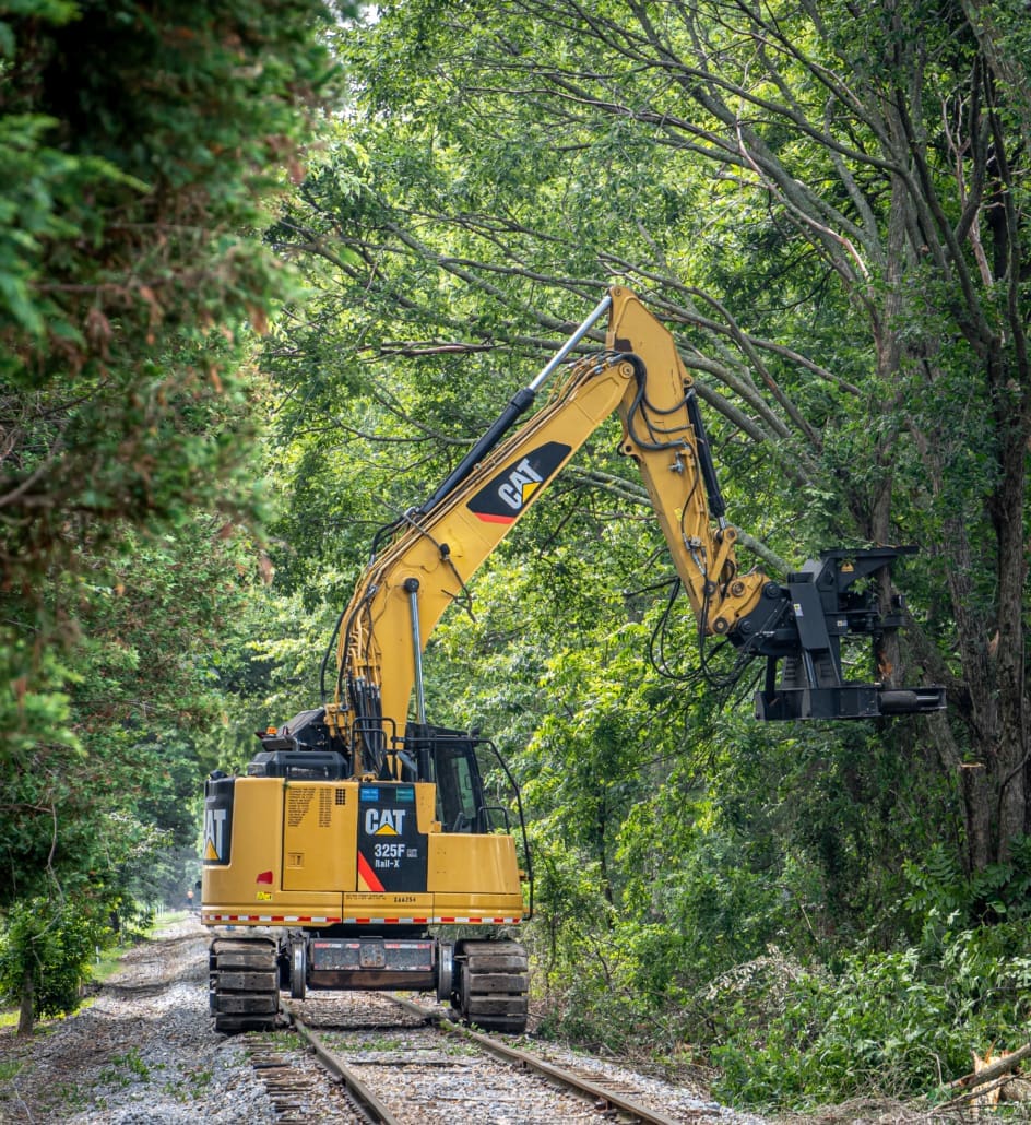 Click to show details - Dymax HPX21 Tree Shear on Cat Excavator – Railway Vegetation Control Cat excavator using Dymax 21-inch tree shear to trim branches overhanging railroad right-of-way