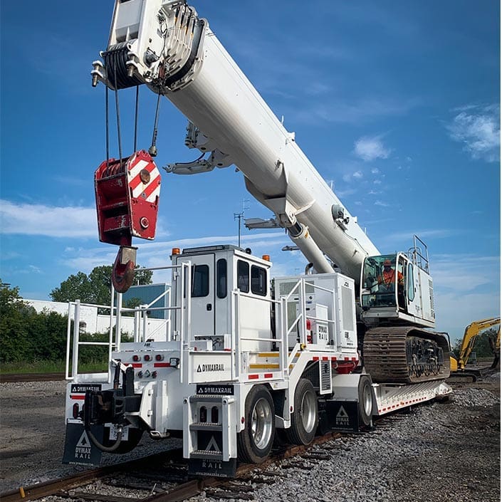 Click to show details - DymaxRail Lowbed 90T Equipment Mover – Crane Transport DymaxRail 90-ton lowbed equipment mover transporting crane on railroad track