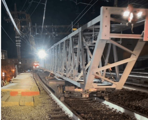 Back end of a large metal structure on a track dolly cart at night. It is rolling away from the viewer.